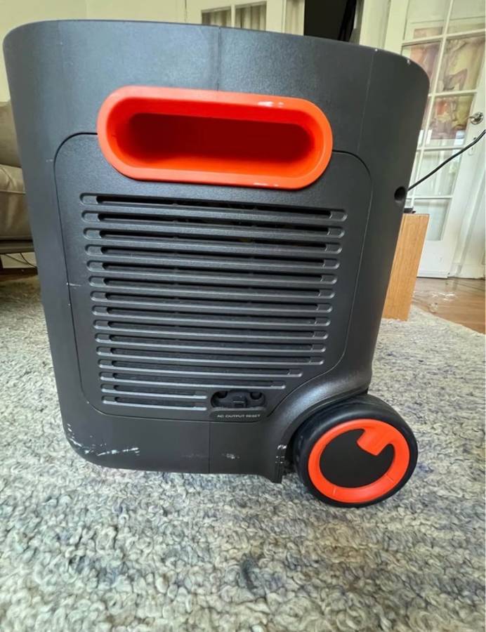 Jackery Explorer 2000 Plus side profile with cooling vents, orange handle and wheel on a living room carpet